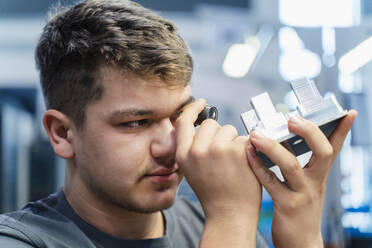 Junger Ingenieur bei der Untersuchung eines kleinen Mikroskops während der Arbeit in der Industrie - DIGF13763