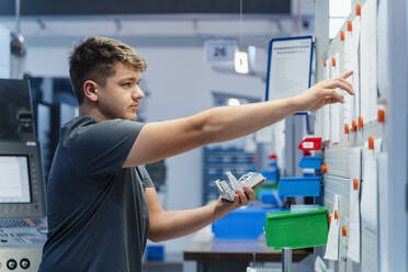 Young engineer reading paper on whiteboard while standing at industry - DIGF13765