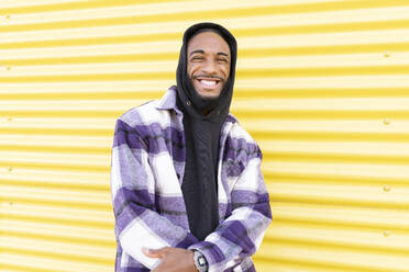 Smiling male rapper standing against yellow corrugated wall - JCCMF00337