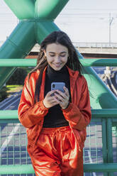 Lächelnde Frau, die auf einer Brücke stehend ein Mobiltelefon benutzt - JRVF00012