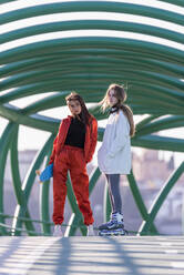Teenager-Mädchen mit Rollschuhen steht mit einem Freund auf einer Brücke - JRVF00033
