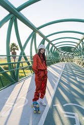 Junge Frau mit Skateboard auf einer Brücke stehend - JRVF00049