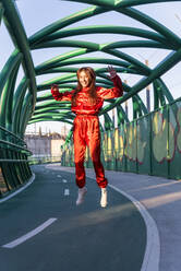 Carefree woman smiling while jumping on bridge - JRVF00057