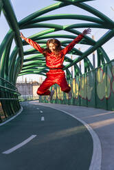Frau im Trainingsanzug springt mit ausgestrecktem Arm auf eine Brücke - JRVF00058