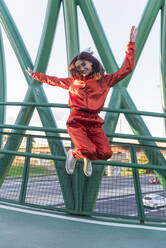 Happy woman jumping with hand raised on bridge - JRVF00059