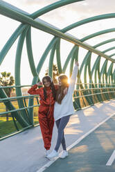 Carefree friends wearing headphones standing on bridge - JRVF00065