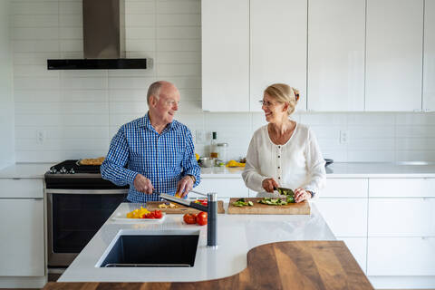 Senior couple talking while chopping vegetables on kitchen island at home stock photo