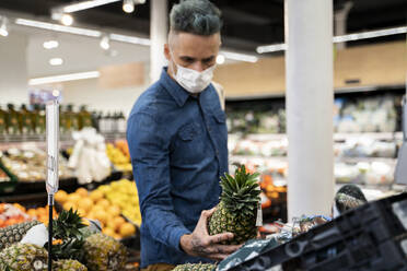Mid adult man wearing face mask buying pineapple in supermarket - AFVF07949