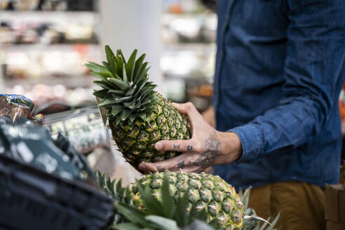 Mittelteil eines erwachsenen Mannes, der im Supermarkt Ananas kauft - AFVF07950