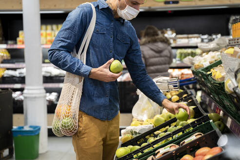 Mittelteil eines Mannes mit Gesichtsmaske beim Kauf von Granny-Smith-Äpfeln im Supermarkt - AFVF07952