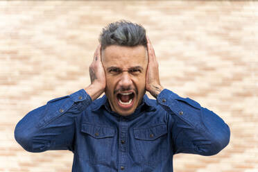 Frustrierter Mann hält sich die Ohren zu und schreit gegen die Wand - AFVF07962