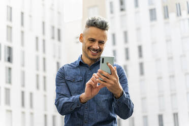 Glücklicher Mann benutzt Smartphone gegen Gebäude - AFVF07966