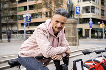 Stylish mid adult man sitting on bicycle against building in city - AFVF07985