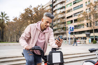 Stilvoller erwachsener Mann, der in der Stadt ein Fahrrad mit Mobiltelefon mietet - AFVF07986