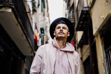 Nachdenklicher stilvoller Mann, der einen Hut trägt, während er vor einem Gebäude in der Stadt steht - AFVF07990