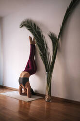 Young woman practicing headstand by wall at home - GRCF00597