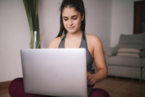 Junge Frau benutzt einen Laptop, während sie zu Hause im Wohnzimmer sitzt, lizenzfreies Stockfoto