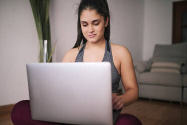 Junge Frau benutzt einen Laptop, während sie zu Hause im Wohnzimmer sitzt - GRCF00600
