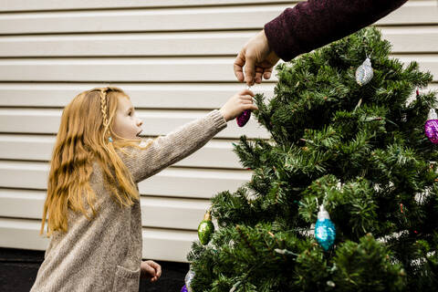 Hand of father assisting daughter in decorating Christmas tree in yard stock photo