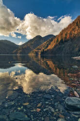 Wolken und umliegende Berge spiegeln sich im Ritsa-See in der Abenddämmerung, Abchasien, Georgien - KNTF06116