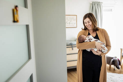 Lächelnde Mutter mit neugeborenem Baby im Kinderzimmer stehend - AWAF00013