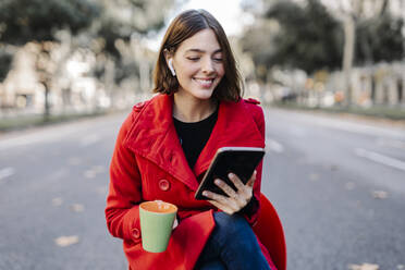 Lächelnde, modische junge Frau mit Kaffeetasse und digitalem Tablet auf der Straße - JCZF00362
