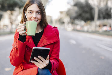 Modische junge Frau, die auf der Straße einen Kaffee trinkt und ein digitales Tablet hält - JCZF00364