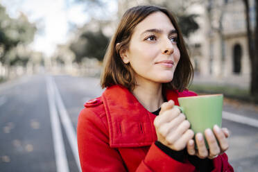 Junge Frau mit Kaffeetasse, die auf der Straße steht und träumt - JCZF00395