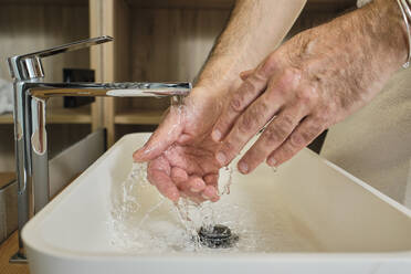 Reifer Mann beim Händewaschen unter fließendem Wasser im Badezimmer zu Hause - AODF00152