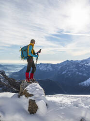Male hiker using smart phone while standing on snowy mountain against sky, Orobic alps, Lecco, Italy - MCVF00695