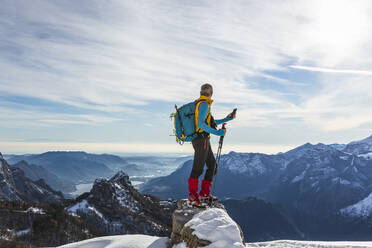Männlicher Wanderer, der sein Smartphone benutzt, während er im Winter auf einem Berg gegen den Himmel steht, Orobische Alpen, Lecco, Italien - MCVF00696