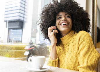 Smiling woman talking on mobile phone while sitting at cafe - JCCMF00359