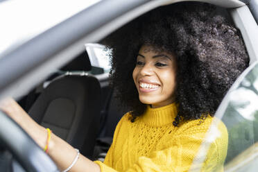 Frau mit lockigem Haar lächelt beim Autofahren - JCCMF00393