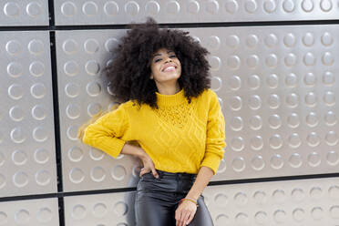 Smiling woman standing with hand on hip against silver wall - JCCMF00414