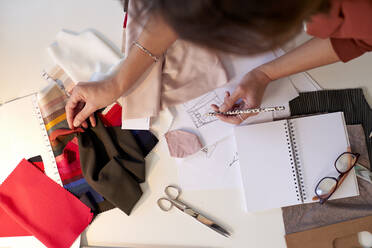 Weibliche Designerin beim Zeichnen und Prüfen eines Stoffmusters am Schreibtisch im Atelier - VEGF03425