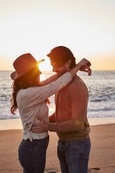 Young couple dancing while standing on beach during sunrise - VEGF03463