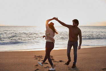 Happy young couple dancing while standing at beach during sunrise - VEGF03469