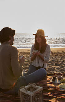 Junges Paar trinkt am Strand sitzend Kaffee - VEGF03476