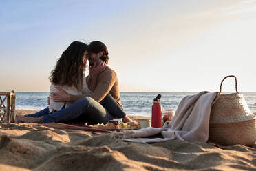 Girlfriend and boyfriend romancing while sitting face to face on beach - VEGF03485