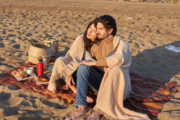 Junges Paar mit Decke, das am Strand sitzt und sich ausruht - VEGF03491