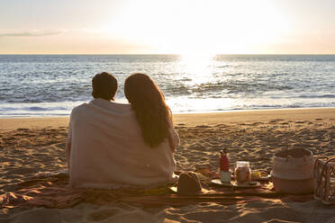 Junges Paar in Decke gehüllt am Strand sitzend und die Aussicht betrachtend - VEGF03492
