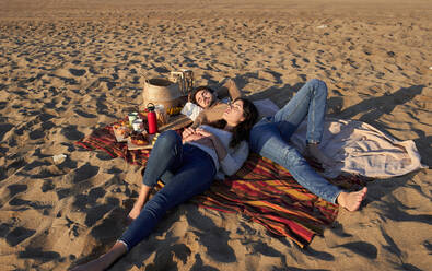 Junges Paar ruht sich auf einer Decke am Strand aus - VEGF03499