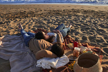 Paar liegt auf einer Decke und ruht sich am Strand aus - VEGF03500