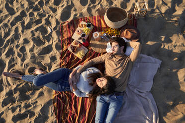 Freundin und Freund liegen auf einer Decke und ruhen sich am Strand aus - VEGF03501