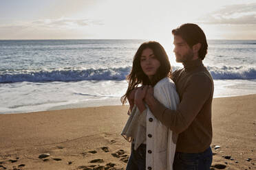 Young man embracing woman while standing against sea - VEGF03506