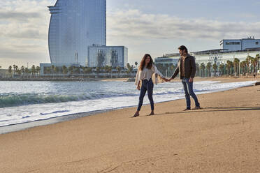 Junges Paar, das am Strand spazieren geht und sich an den Händen hält - VEGF03508