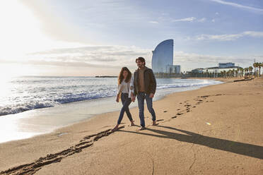Freundin und Freund halten sich an der Hand, während sie am Strand spazieren gehen - VEGF03510