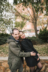 Portrait of cheerful couple standing against plants in park - GRCF00611