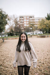 Smiling teenage girl standing on land in park during winter - GRCF00616
