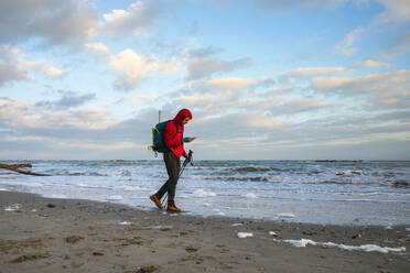 Mann benutzt Smartphone beim Spaziergang am Strand, Mittelmeer, Italien - MCVF00708